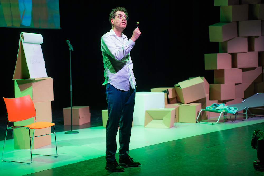 Posterbeeld: Ewald van Kouwen als Maarten met een lolly in zijn hand op het podium, tussen kartonnen dozen